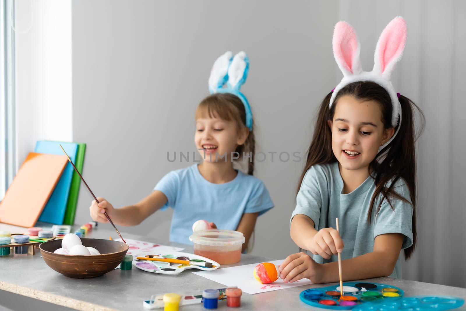 Happy easter. Two sisters painting Easter eggs. Happy family children preparing for Easter. Cute little child girl wearing bunny ears on Easter day. by Andelov13