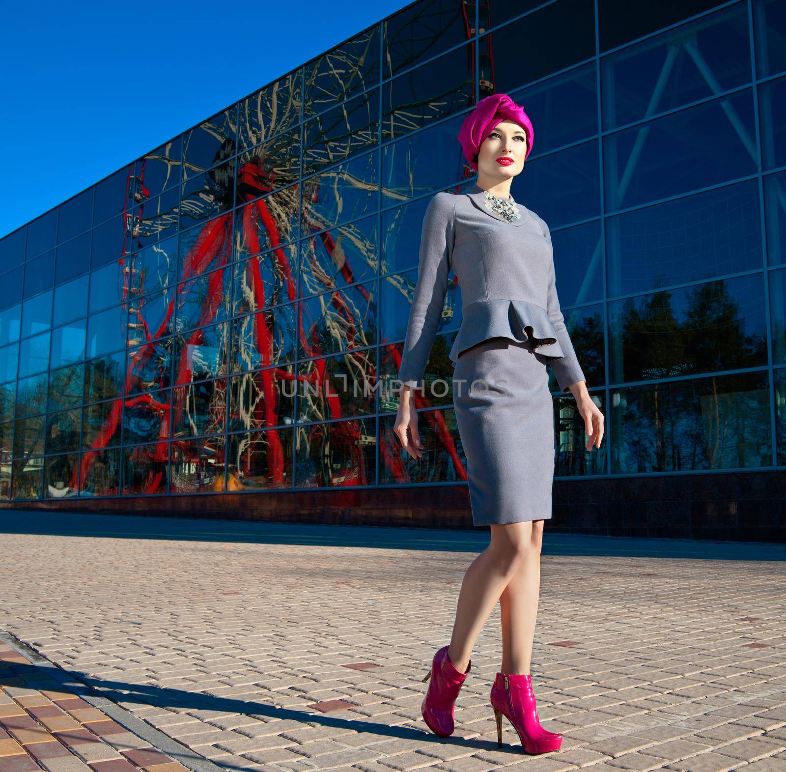 Fashion photo of a beautiful woman in front of a building with reflection of Ferris wheel at summer time