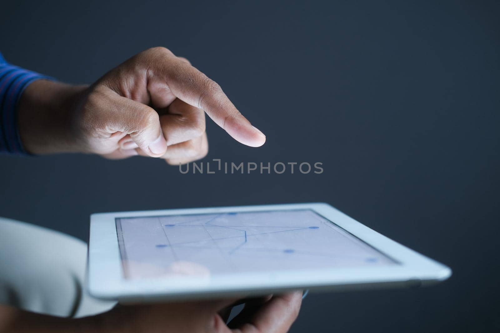 man's hand working on digital tablet at office desk, using self created chart.