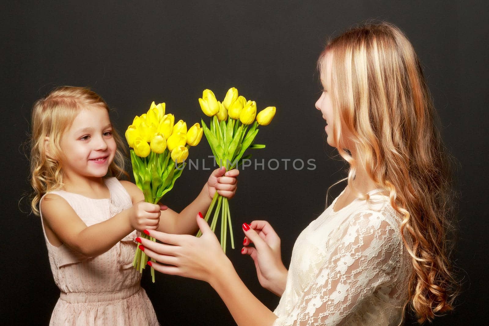 Two beautiful little girls with flowers in the studio. The concept of happy people, children.