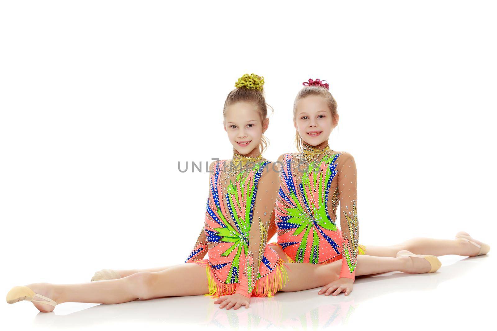 Two adorable little twin girls, gymnastics in the sports school. Girls beautiful gymnastic leotards. They do the splits.Isolated on white background.