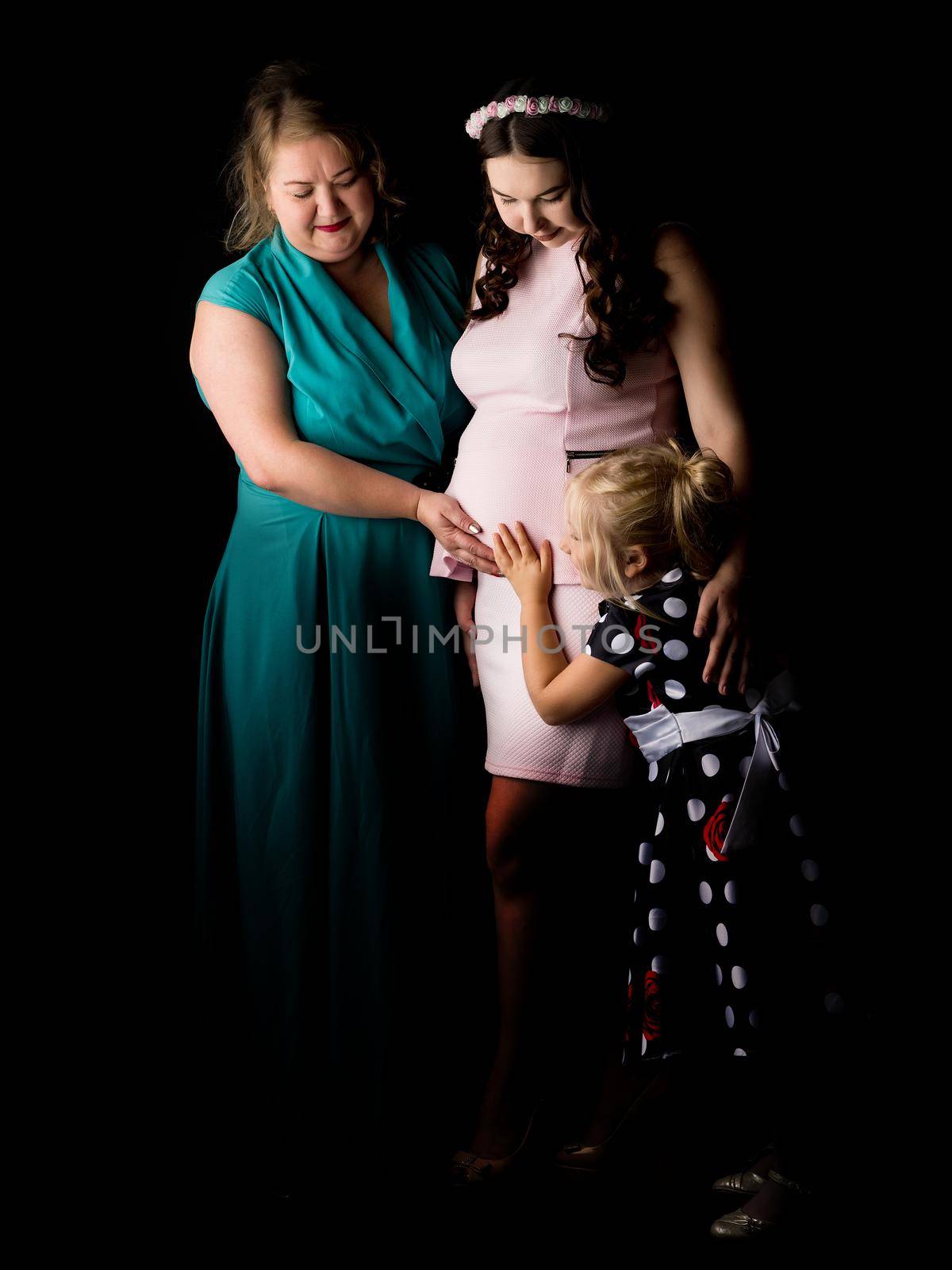 Young pregnant girl with her mother and younger sister on a black background.