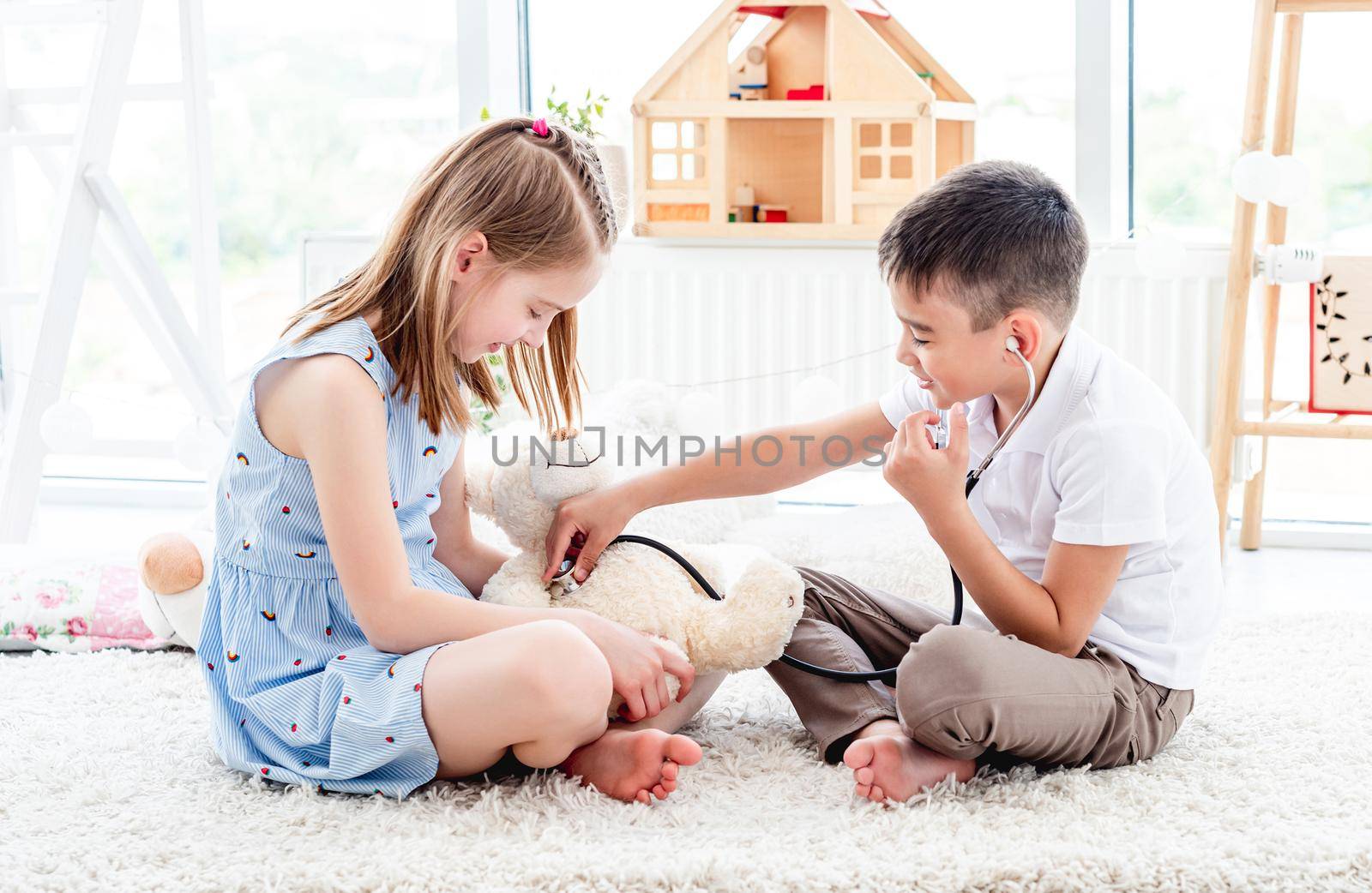 Smiling children playing doctor with teddy bear in bright room