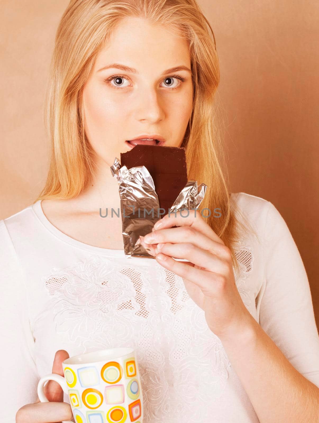 young cute blond girl eating chocolate and drinking coffee close up on warm background
