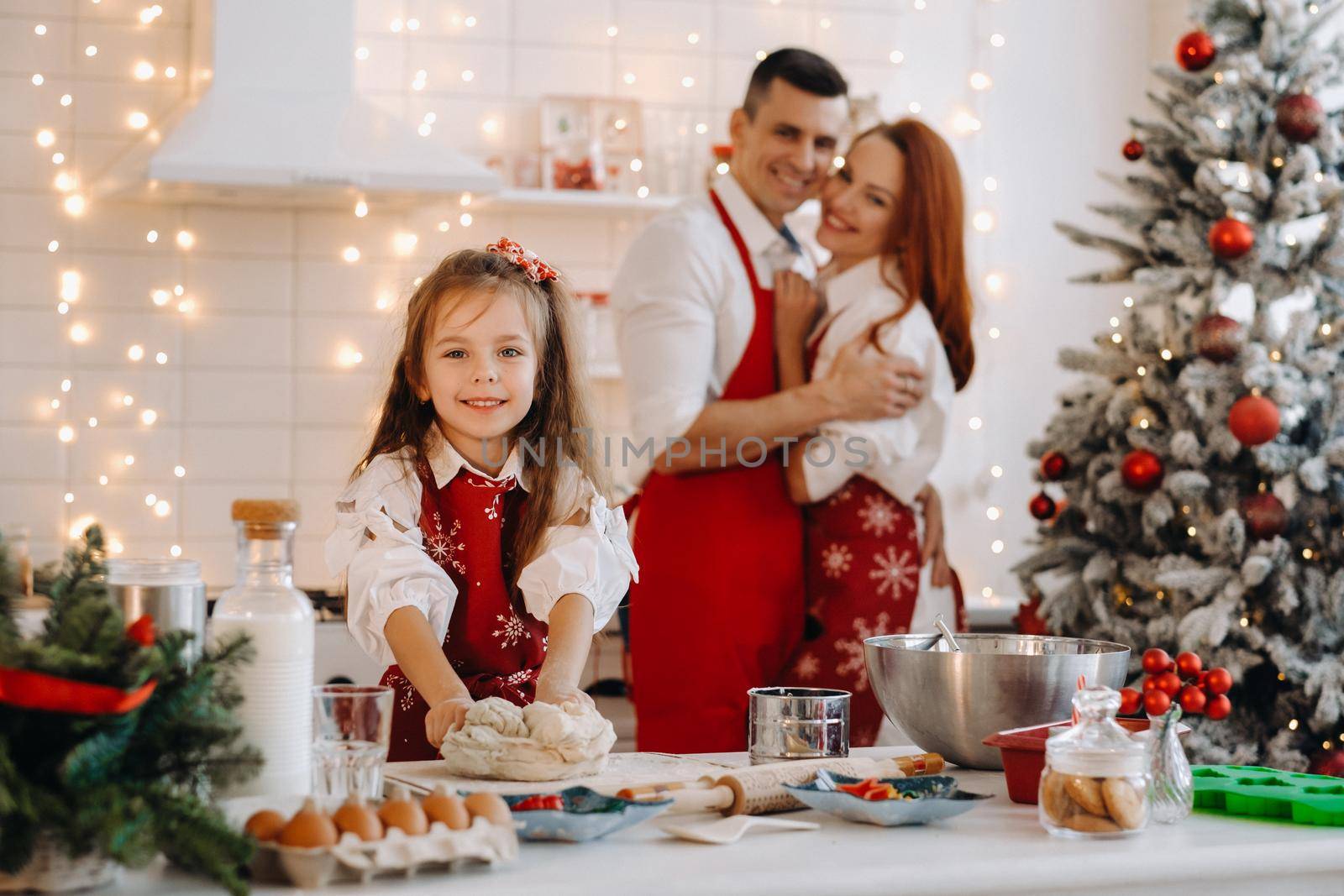 A little girl in the New Year's kitchen makes dough, and her mom and dad are watching next to her.