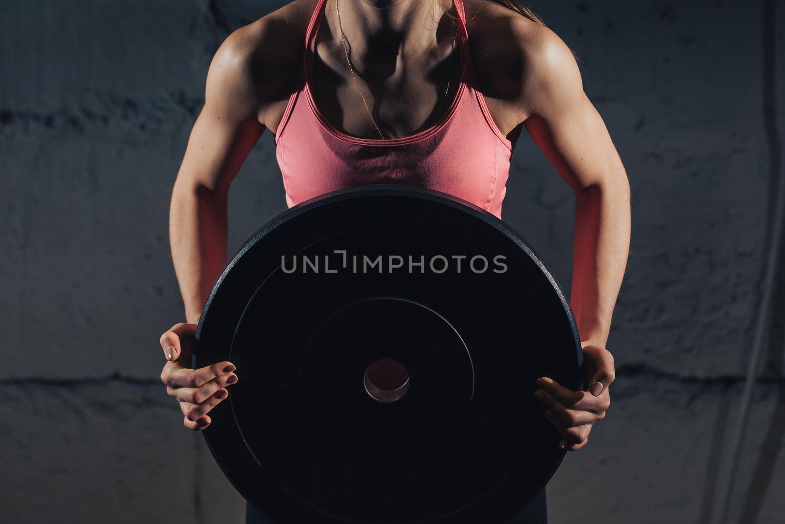 Muscular young fitness woman lifting a weight crossfit in the gym. Fitness woman deadlift barbell. The gym on the red wall is written SPORT. Crossfit woman. Crossfit style. Crossfit and fitness