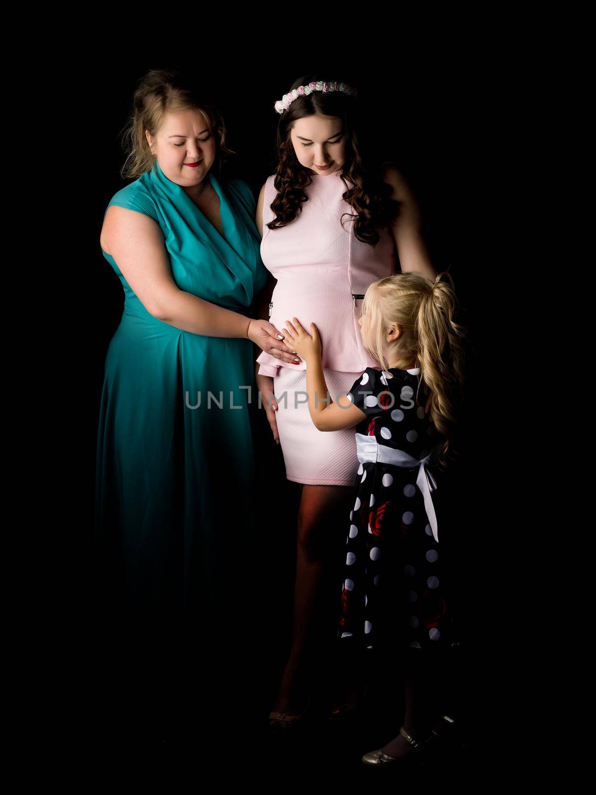 Young pregnant girl with her mother and younger sister on a black background.