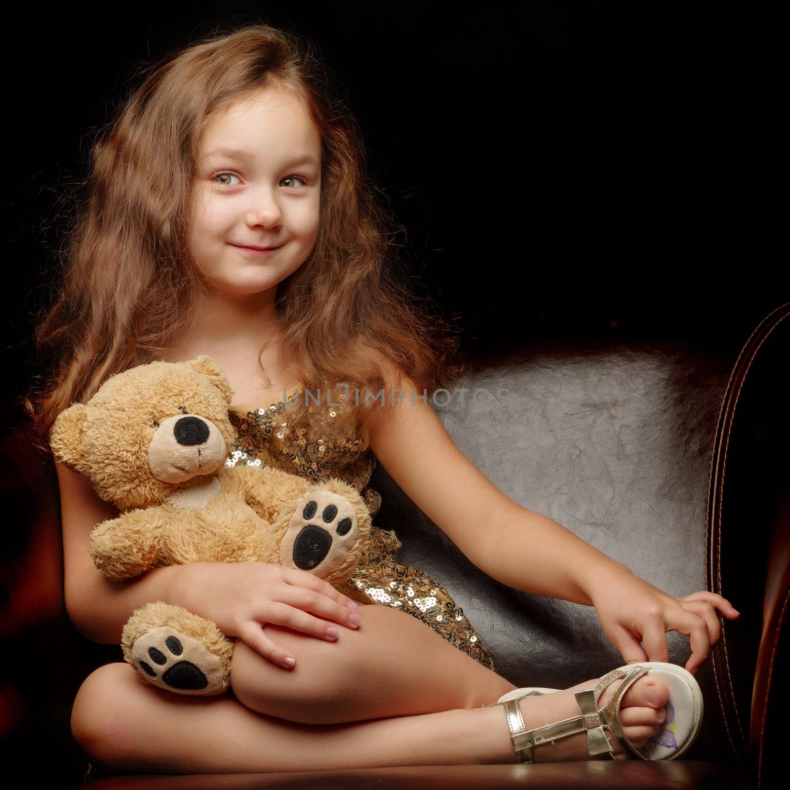 A nice little girl with a teddy bear. Studio photo on a black background. The concept of a happy childhood, publication on the cover of the magazine.