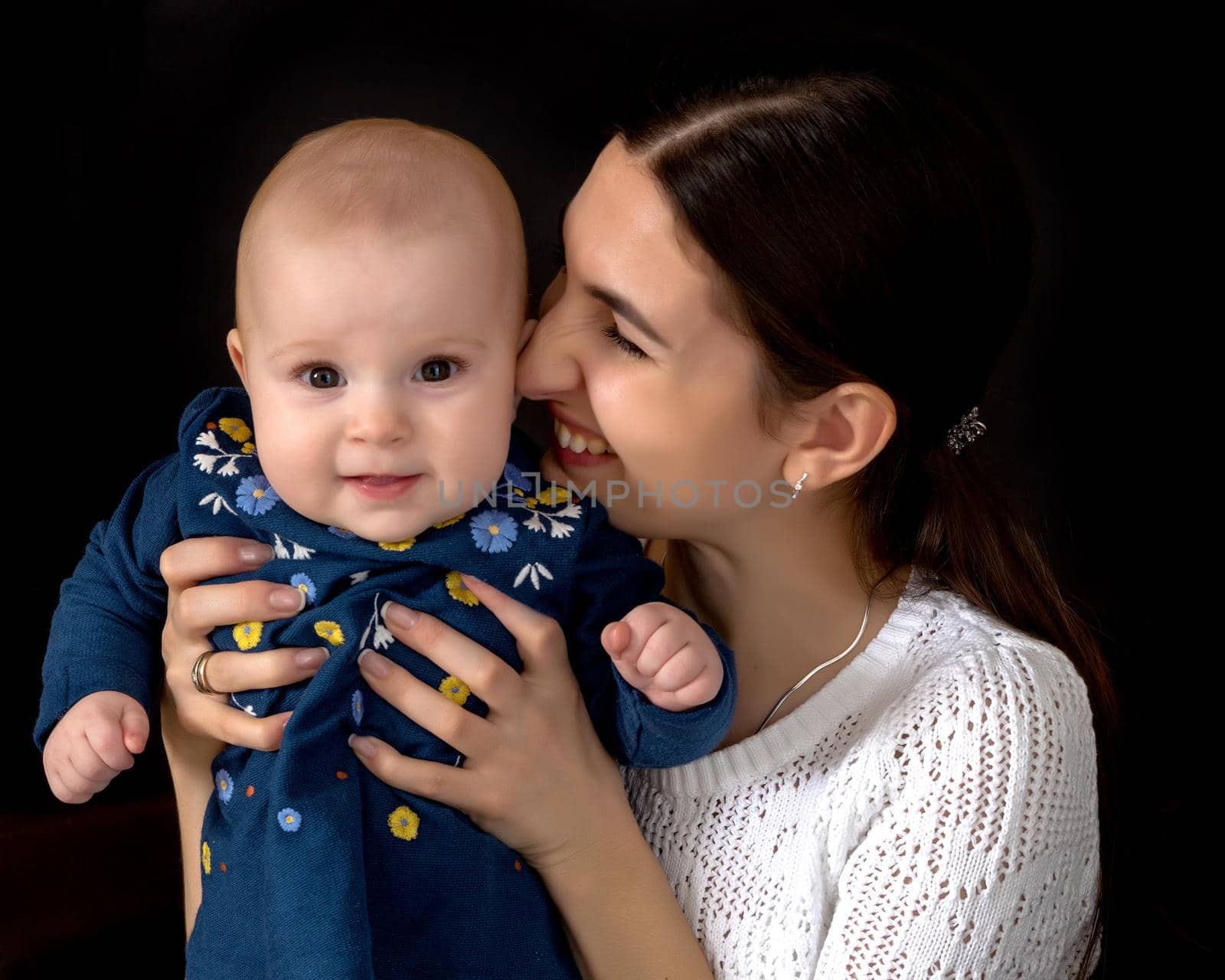 Beautiful young mother with a little daughter in her arms, studio on a black background. The concept of a happy childhood, advertising.