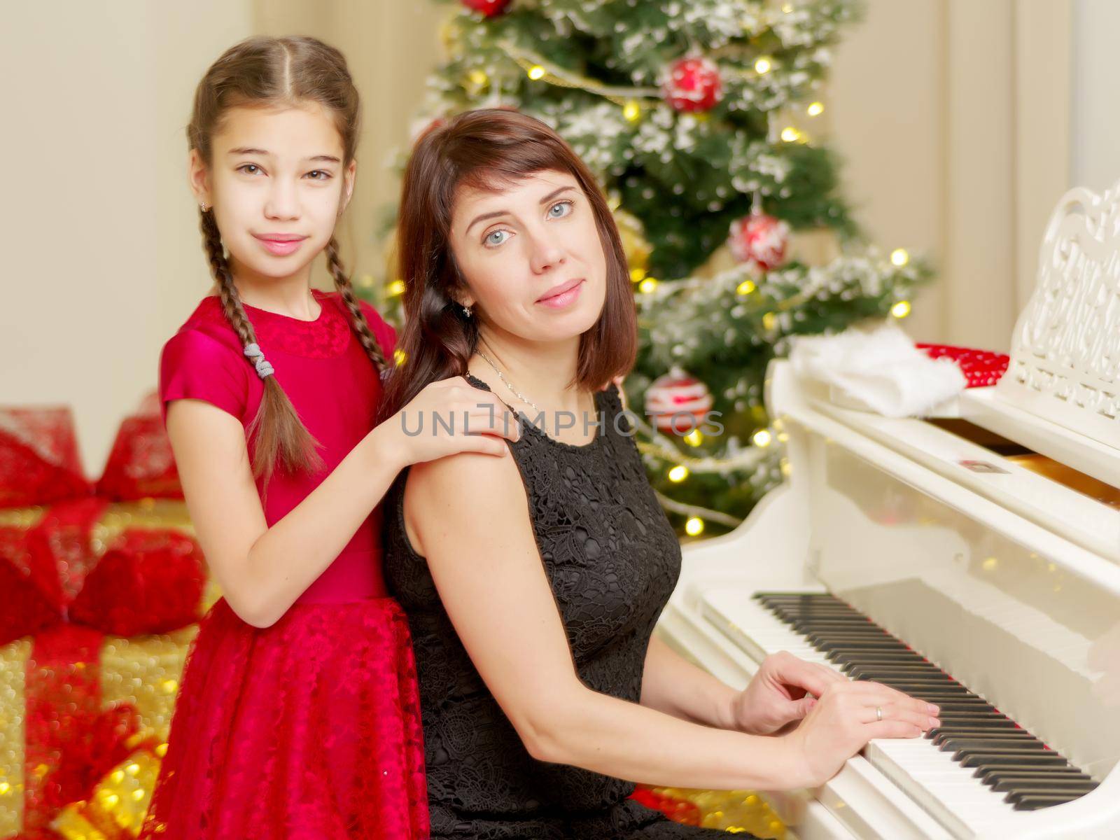 Mom and daughter new years eve near the white piano. Family holidays concept.