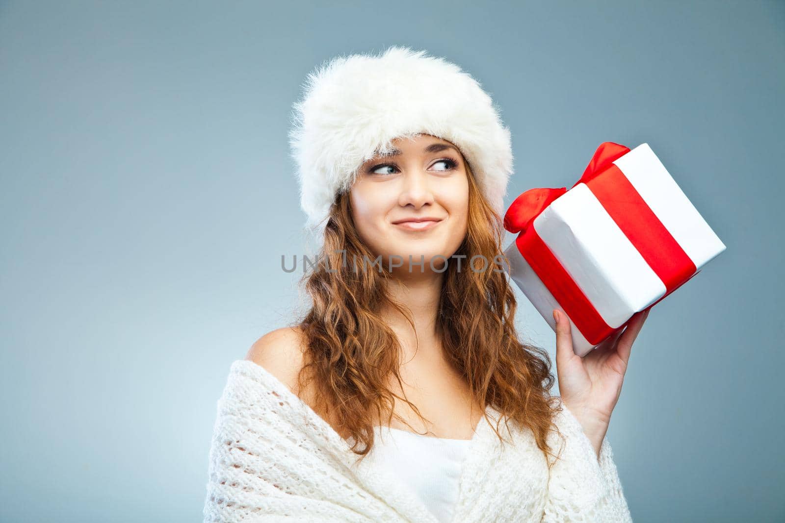 Young attractive girl in Christmas style holding present over grey