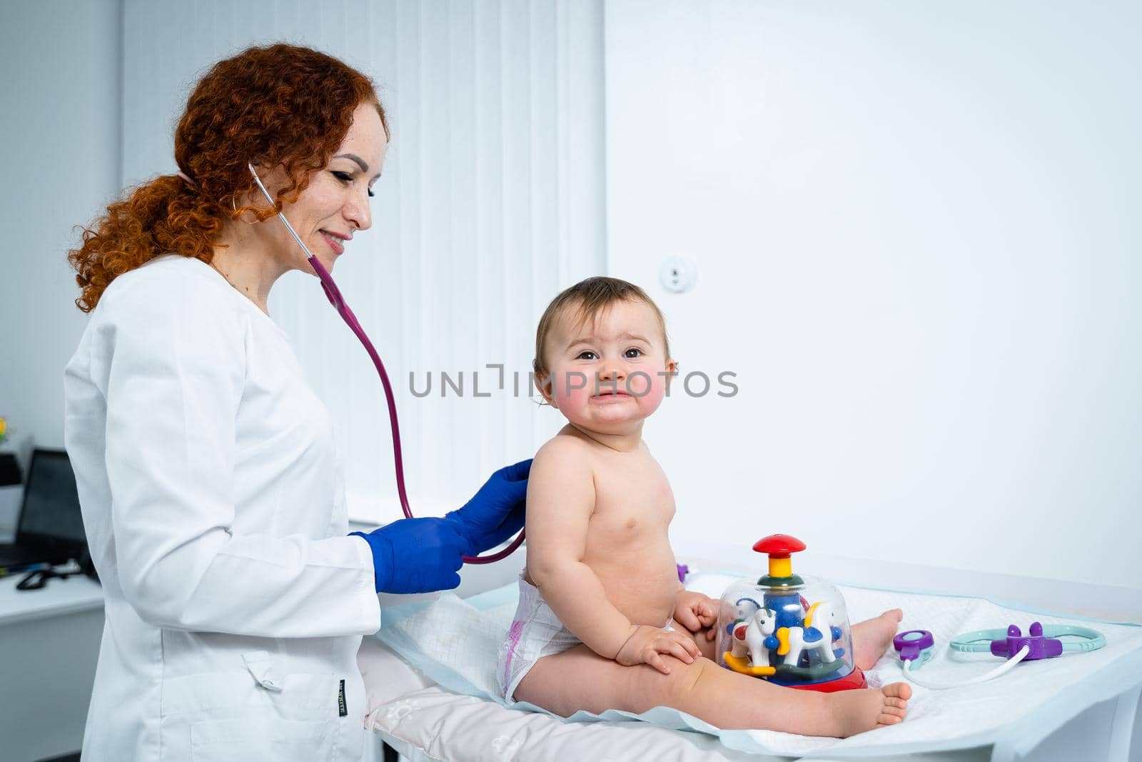 Pediatrician doctor concept. Children medical care. One year old baby girl examined by female pediatrician in clinic office. Child visiting doctor for health check-up. Doctor examine little patient by Tomashevska