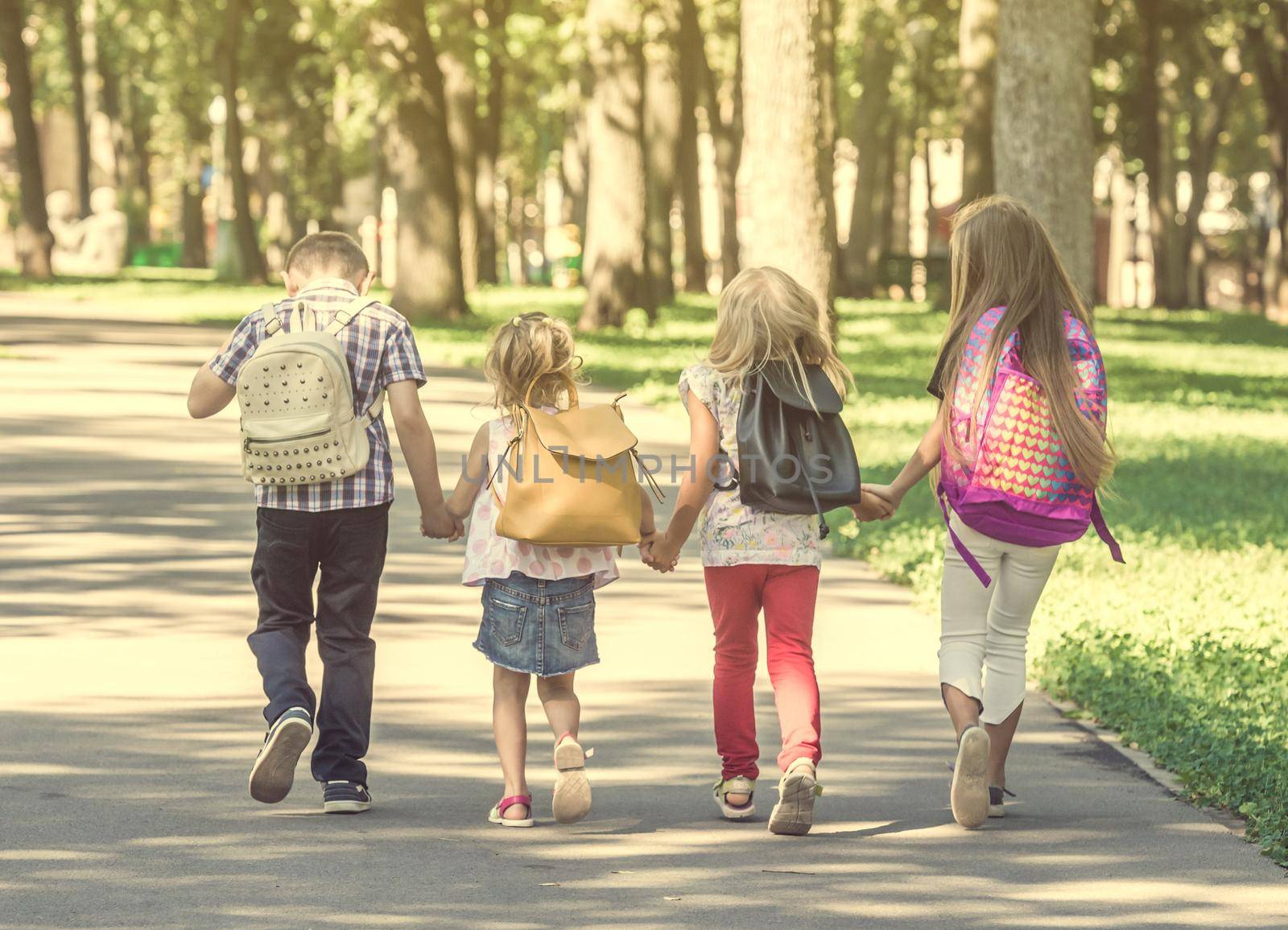 Little pupils walking home from school across the sunshine park
