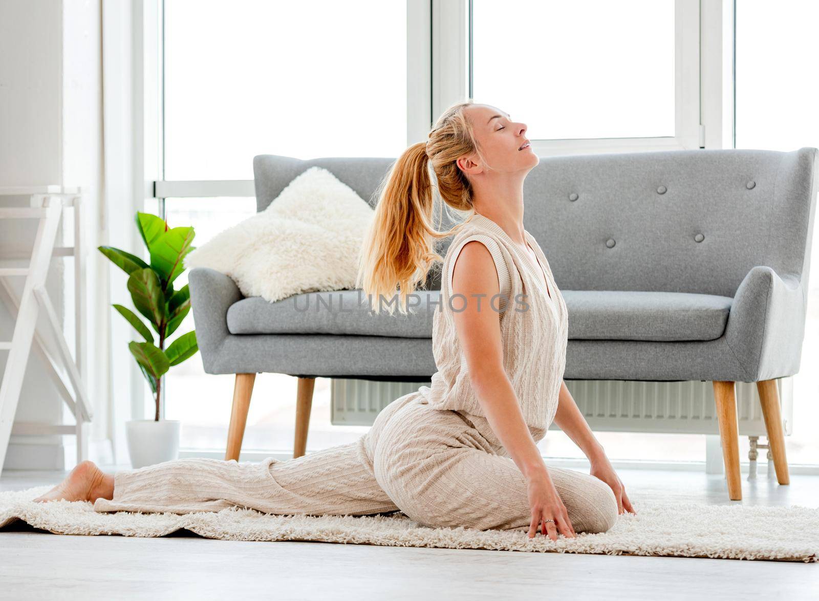 Beautiful blond girl stretch her body during morning yoga workout in the room with sunlight