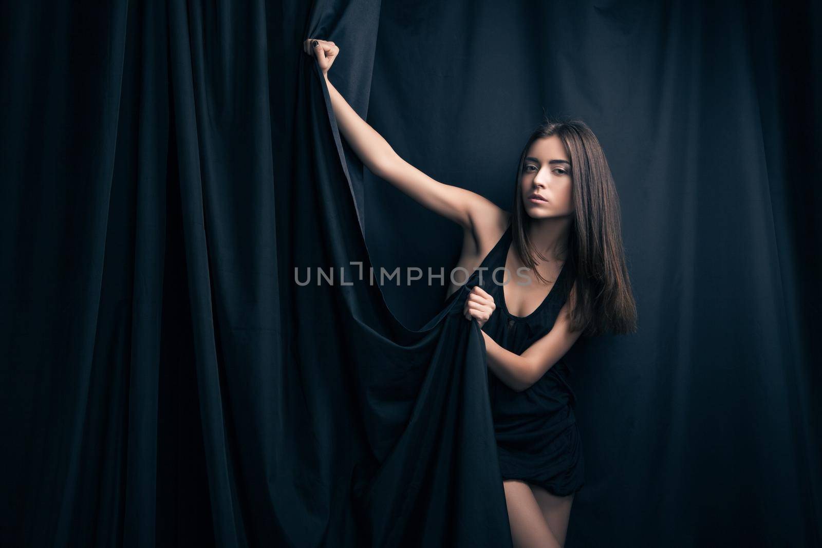Beautiful fashion model posing and foldinng stage curtains. by Julenochek