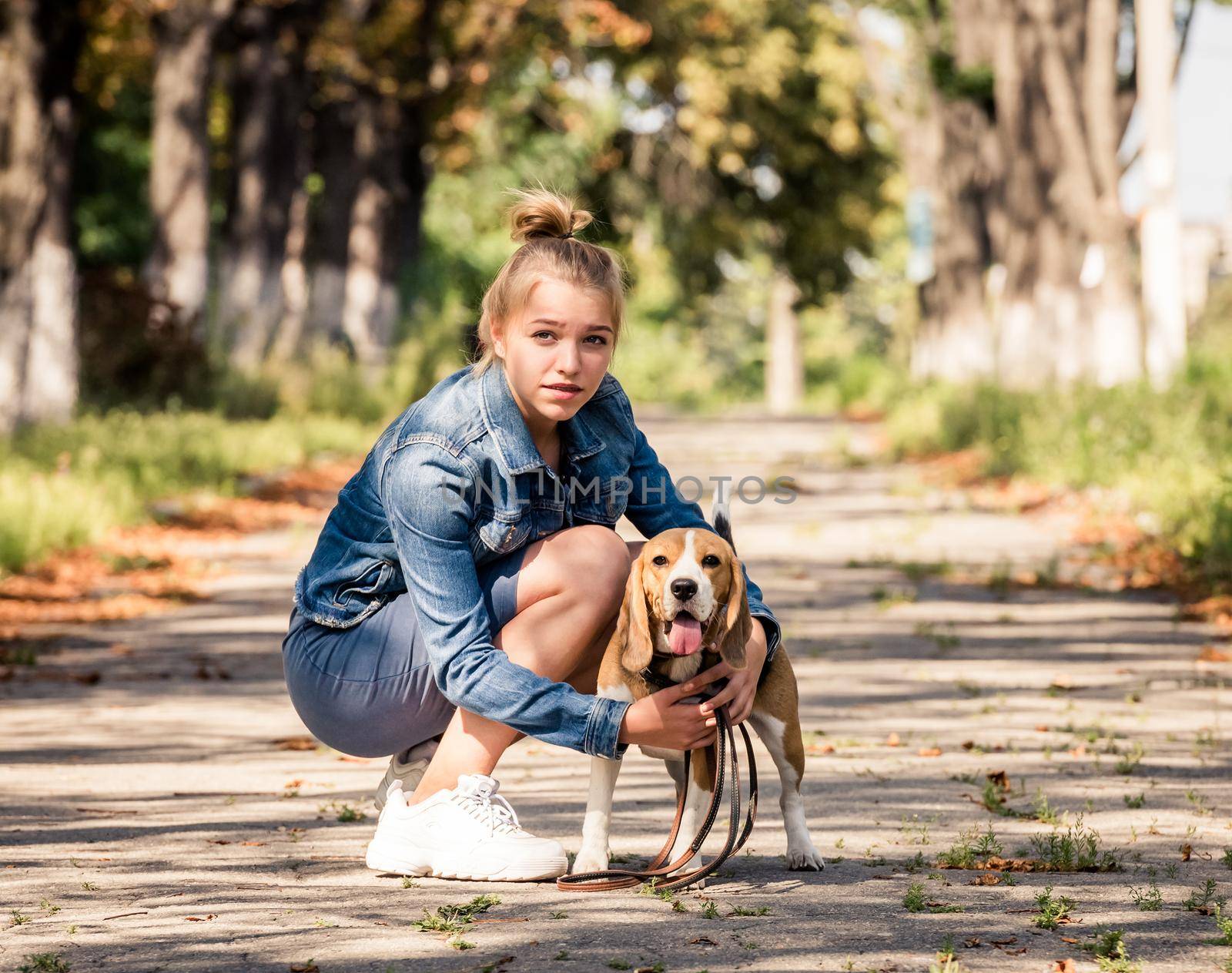 Blond beautiful girl sitting with cute puppy on the sunshine autumn park alley