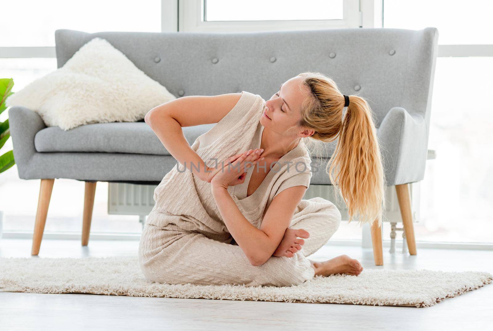 Blond girl sitting in yoga asana on the floor in the room with sunlight. Home stretching workout