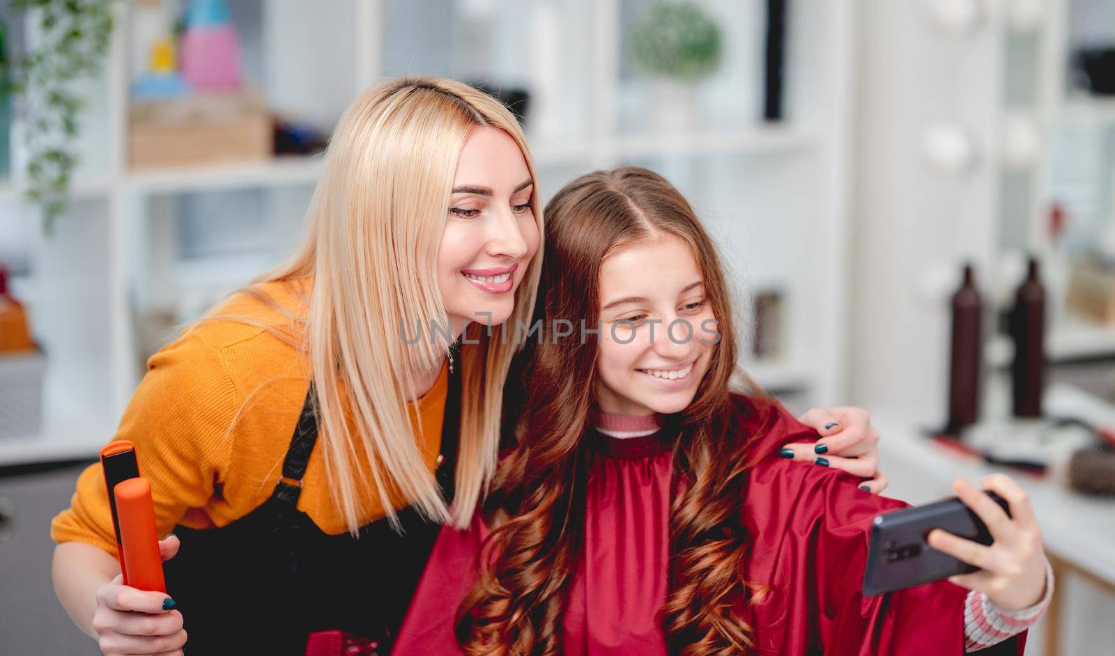 Beautiful girl with long hair curls hairstyle making selfie with hairdresser in salon