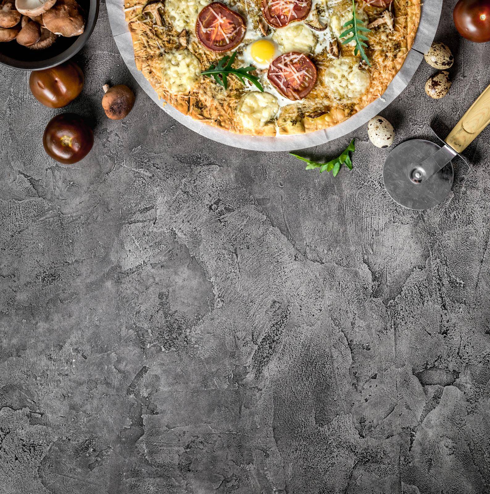 Homemade pizza with mushrooms and mozzarella decorated with arugula on a concrete background with food ingredients. space for text