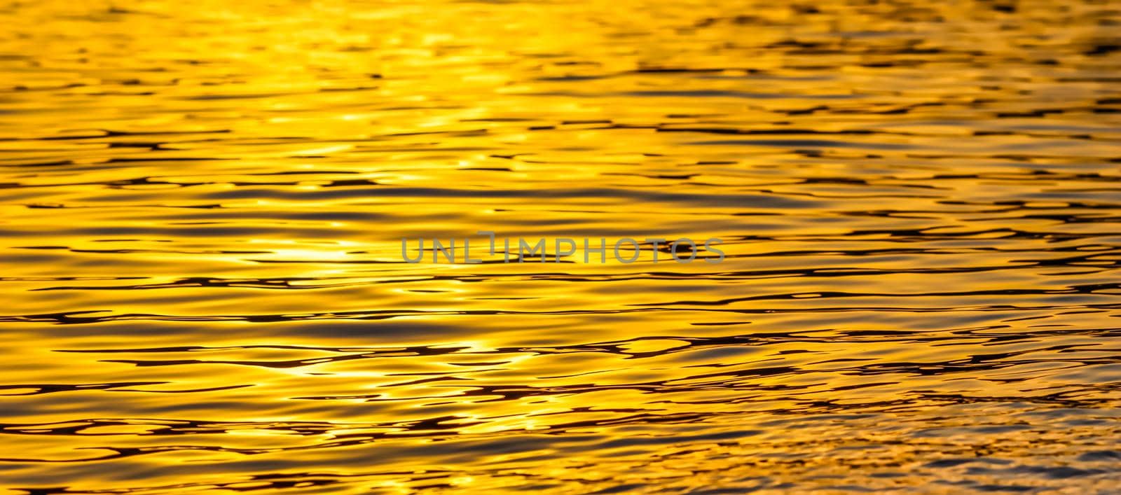 Golden sea waves in sunset glow as surface background. Summer holidays and coastal nature concept