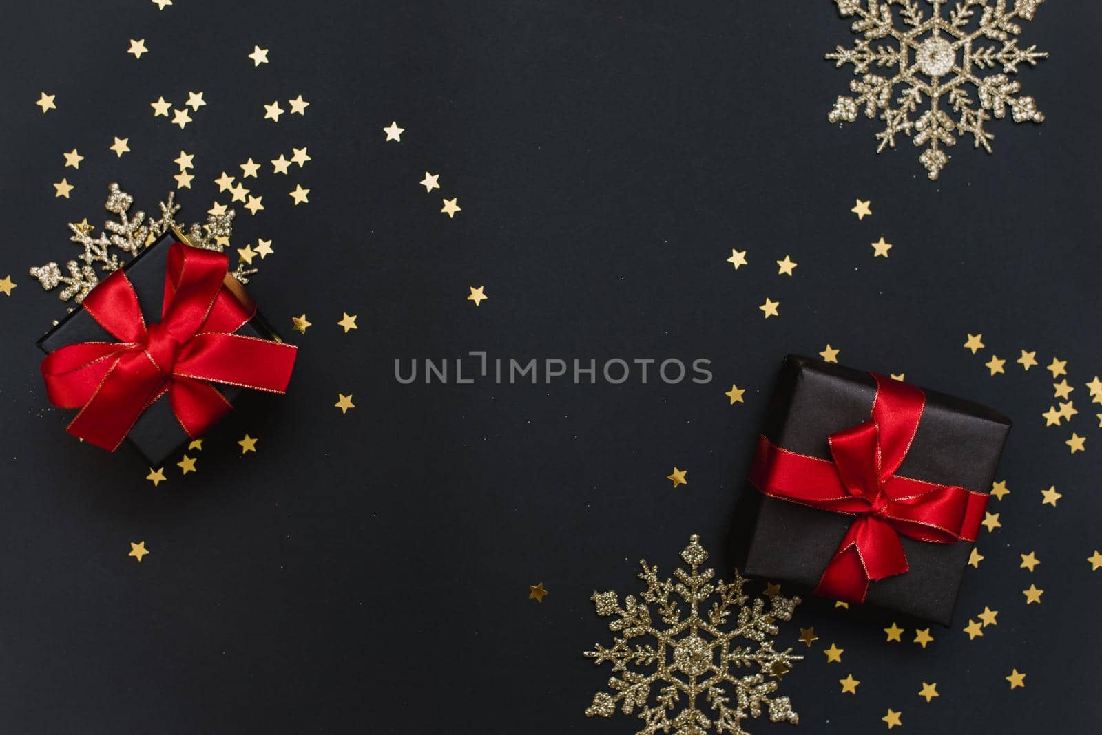 New Year's gifts with red bows on a black background with confetti and gold snowflakes and balls. Preparing for a stylish Christmas party