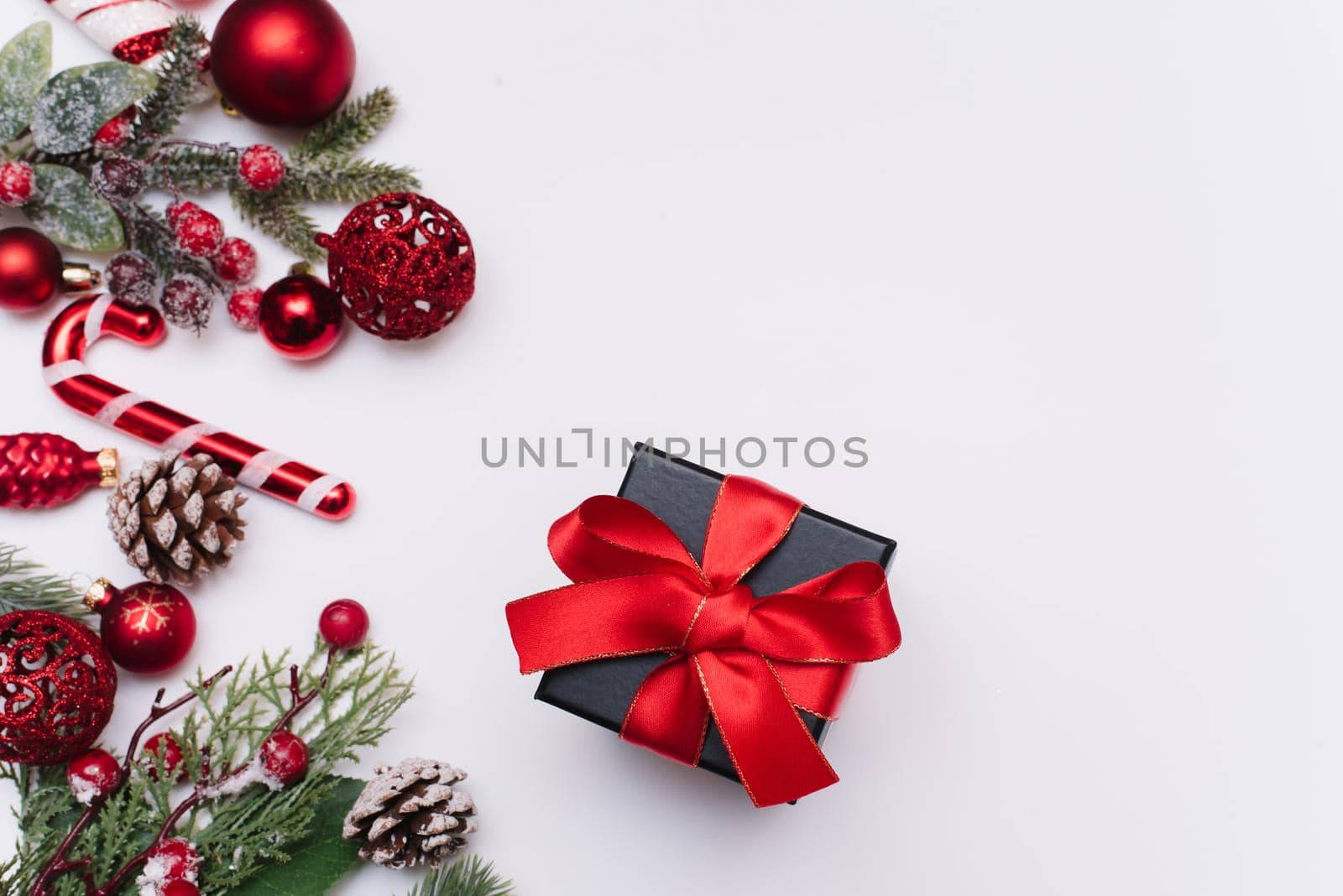 Fir branches with Christmas red decorations and balls around a black gift with red bows on a white background with copy space for text