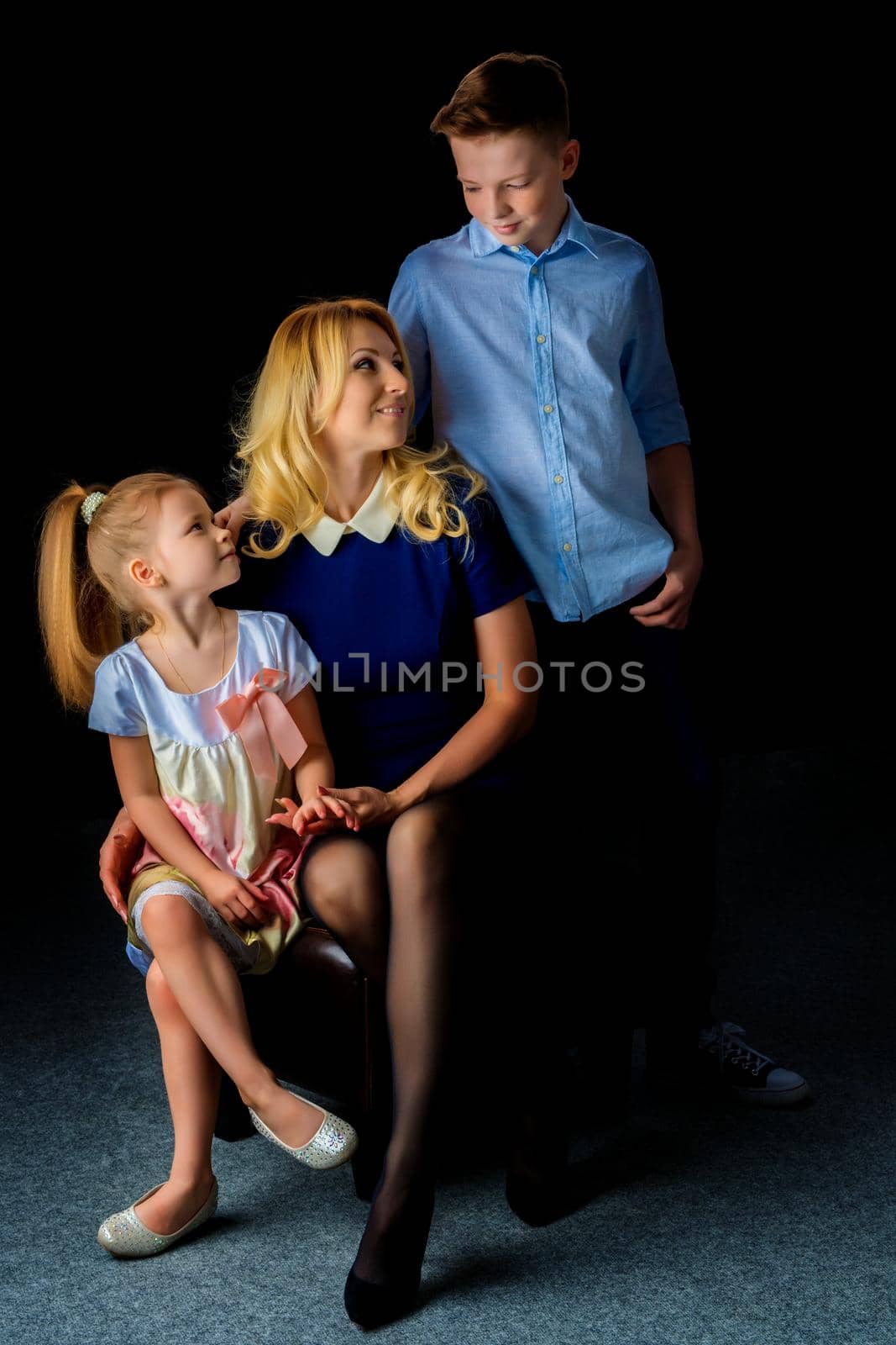 Beautiful young mother with her son and daughter in the studio on a black background. The concept of a family portrait, a friendly family.
