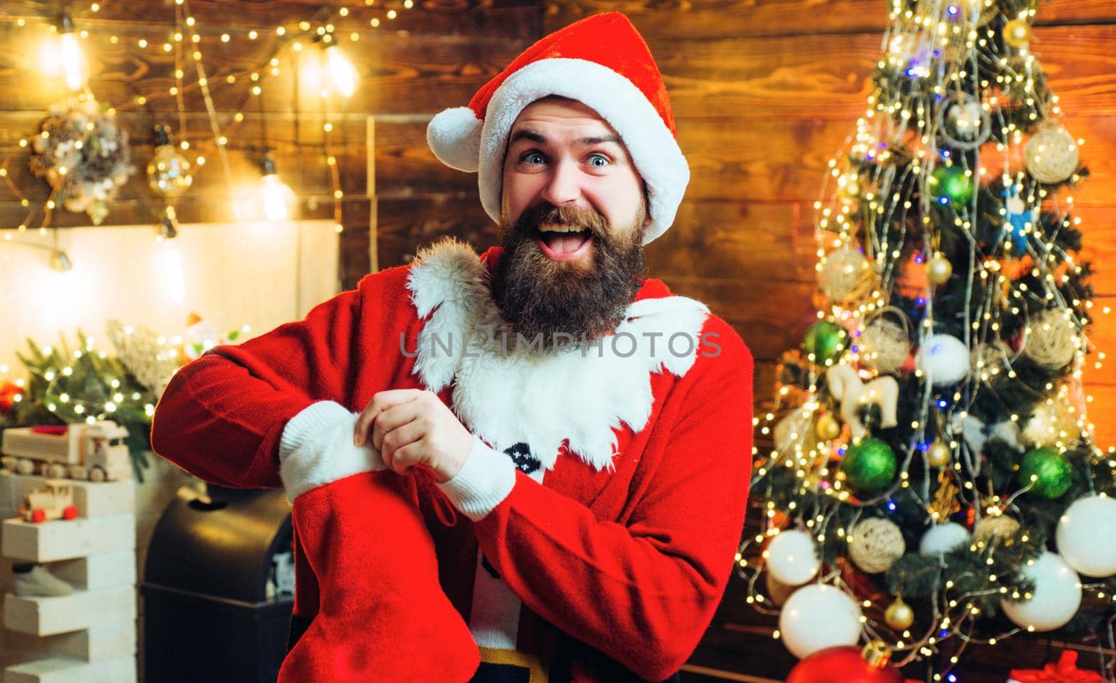Santa hipster with christmas stockings. Man posing on the Christmas wooden background. Winter emotion. by Tverdokhlib