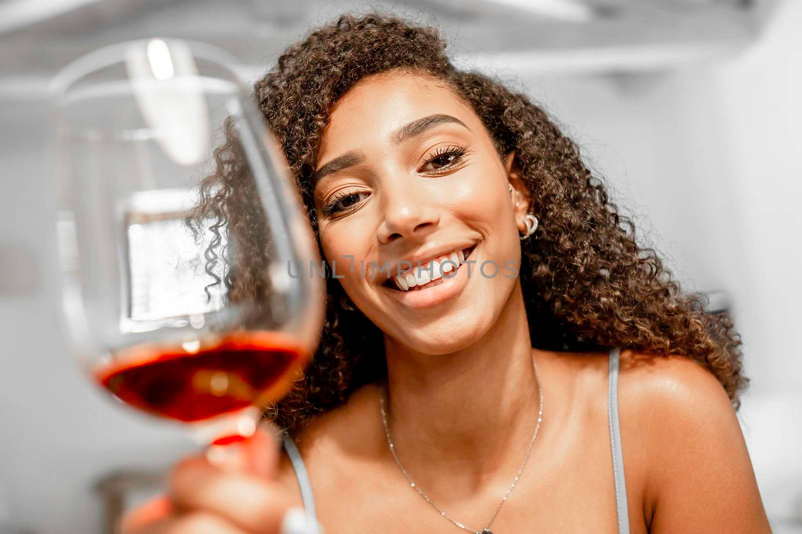 Close-up of young beautiful Afro-American woman toasting looking at camera in video conference POV simulation. New normal celebration online due to social distancing. Black Hispanic girl with red wine by robbyfontanesi