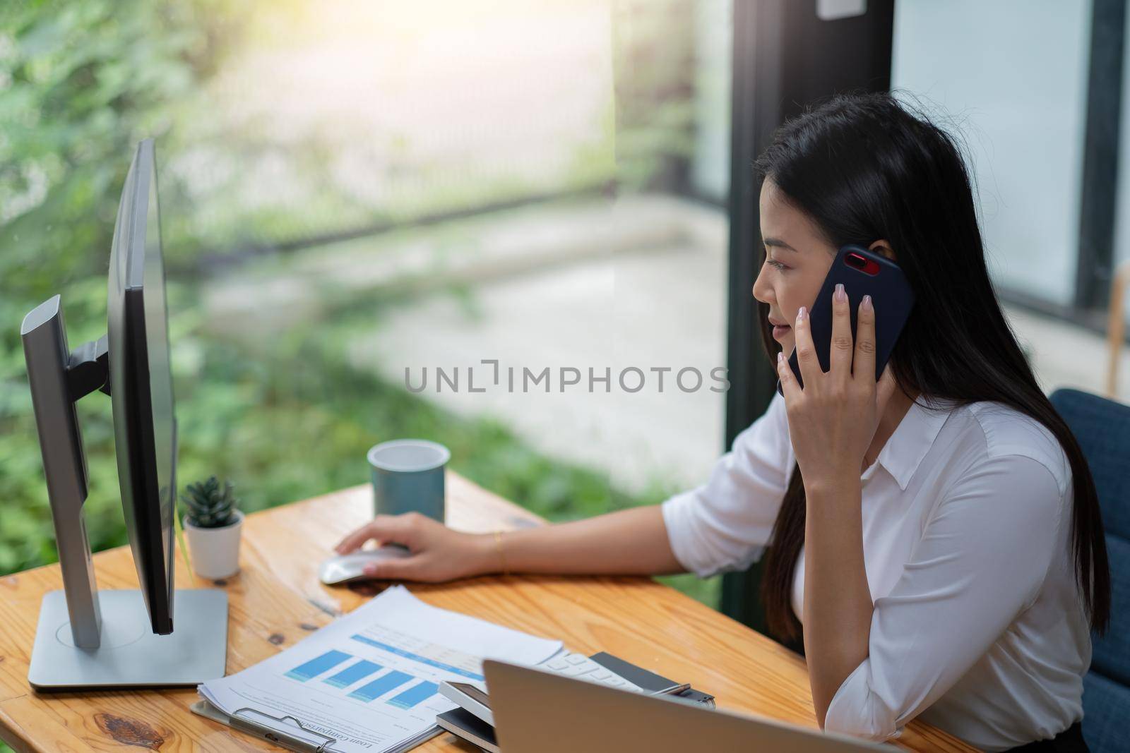 Young asian woman working on laptop at office while talking on phone, business financial concept.