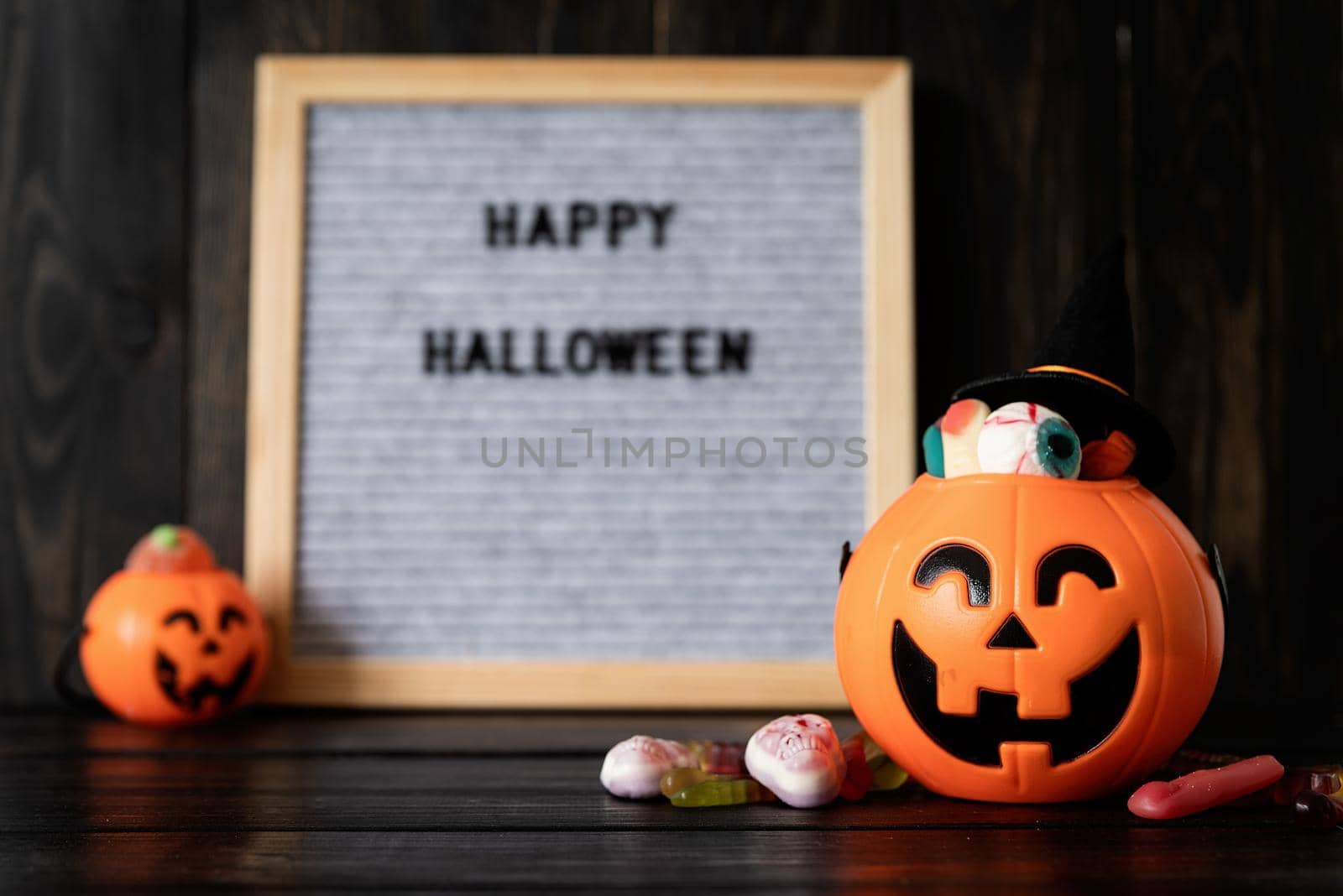 Halloween concept. Halloween party jack o lanterns pumpkins full of sweets on black wooden background, blurred letter board with words Happy Halloween on background