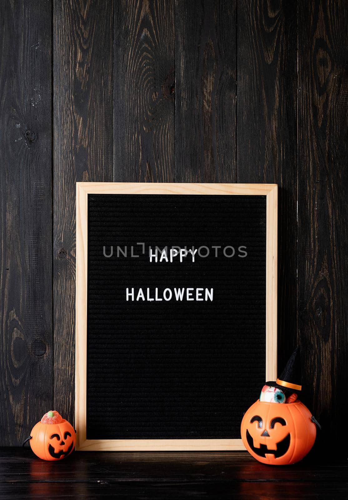 Halloween concept. Halloween party jack o lanterns pumpkins full of sweets on black wooden background, letter board with words Happy Halloween