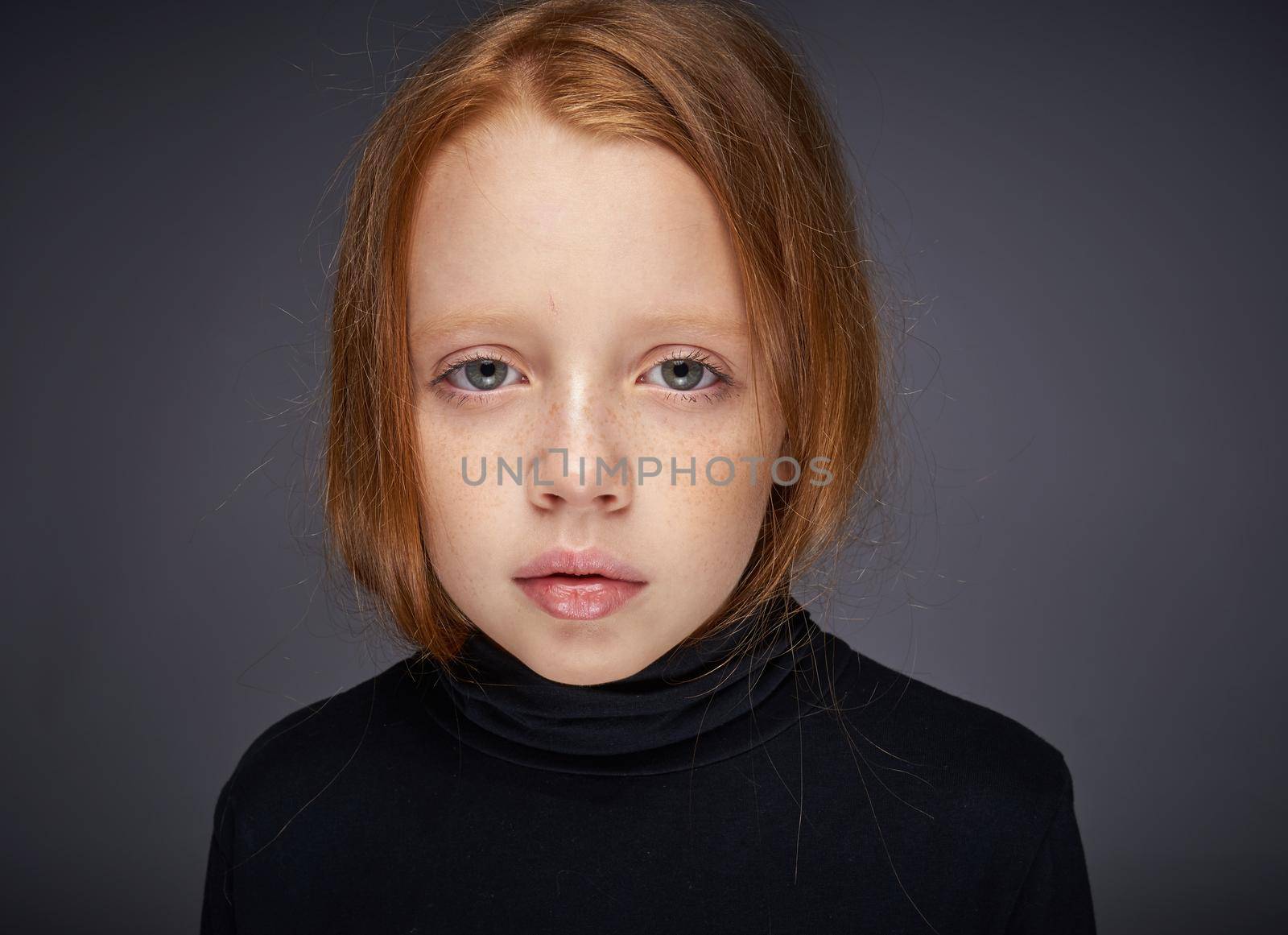 red-haired girl with freckles on her face in a black sweater posing. High quality photo