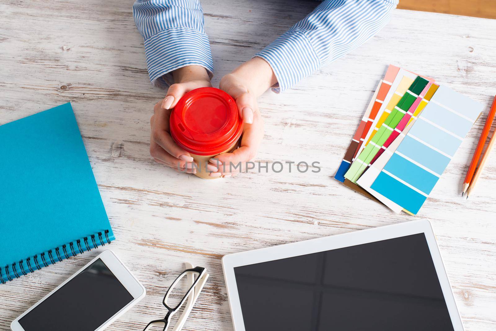 Office manager holding cardboard cup of coffee at wooden desk. Office workspace with tablet computer and accessories. Coffee break at office workplace. Young woman drinking coffee from disposable cup