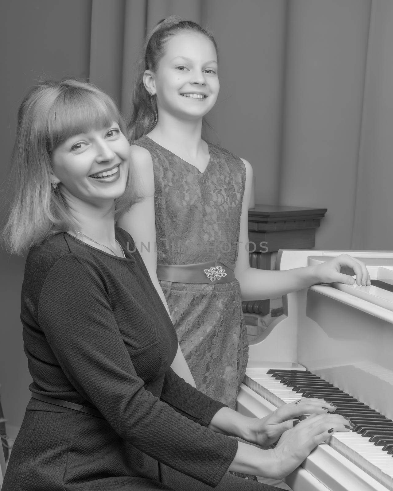 A beautiful young mother with a little daughter near a large white grand piano. The concept of family happiness, music education.