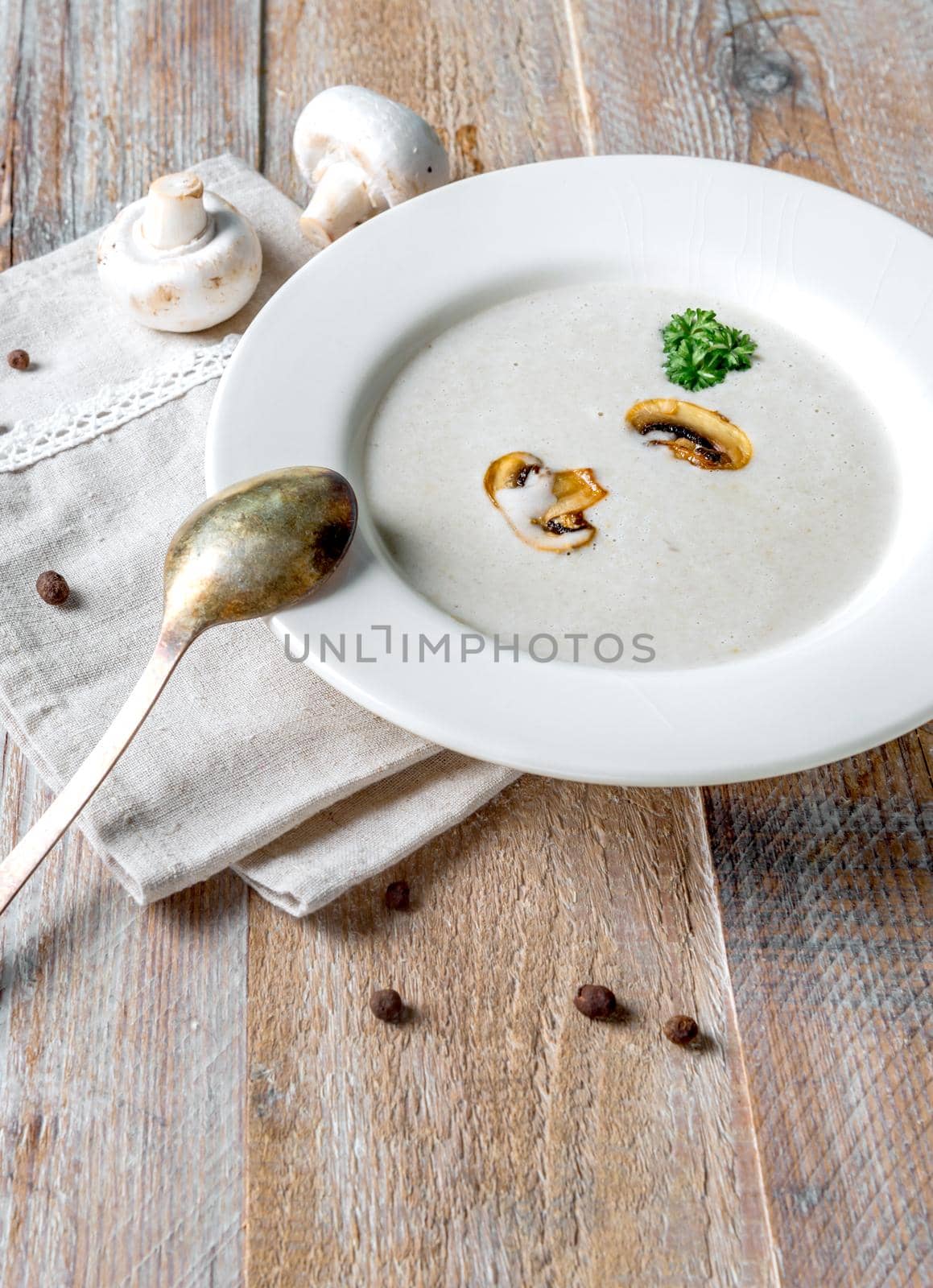 Delicious creamy mushroom soup with some pieces of mushrooms in it, old spoon and napkin