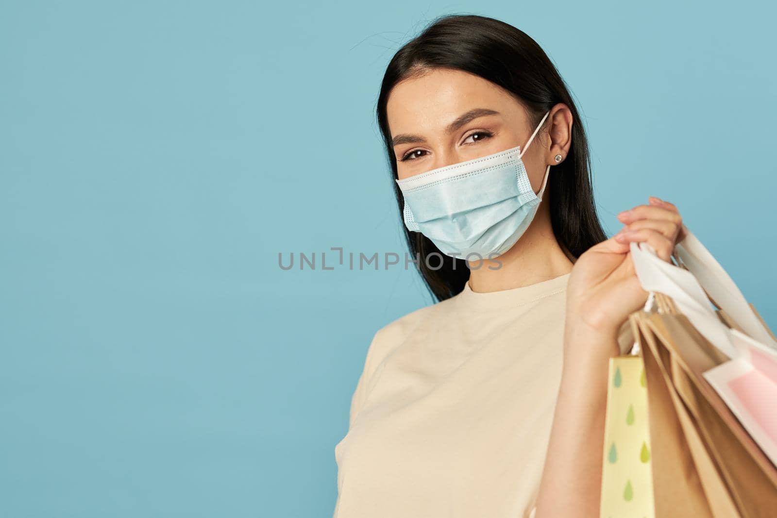 Waist up of pretty woman in disposable face mask holding shopping bags. Copy space. Quarantine, coronavirus concept