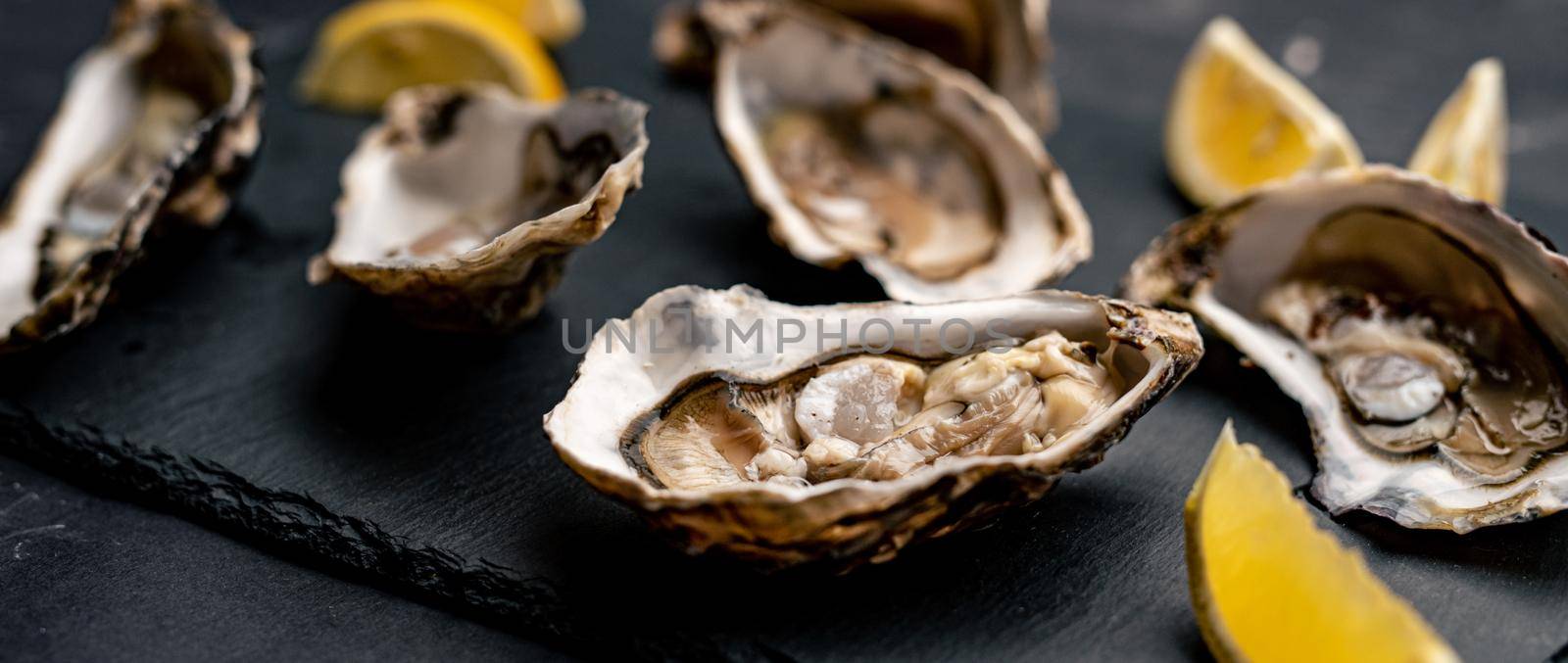 Fresh raw opened oysters served with lemon on balck platter. Seafood delicatessen