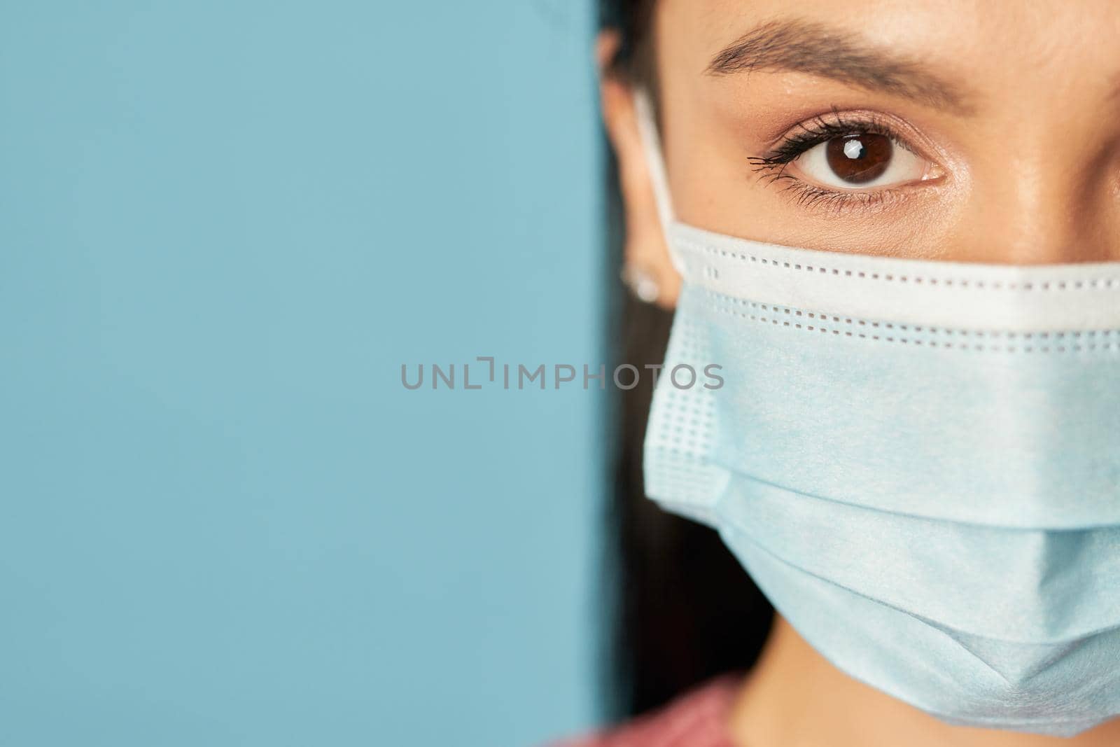 Cropped photo of young woman in a medical mask, isolated on blue wall background. Copy space. Quarantine, coronavirus concept