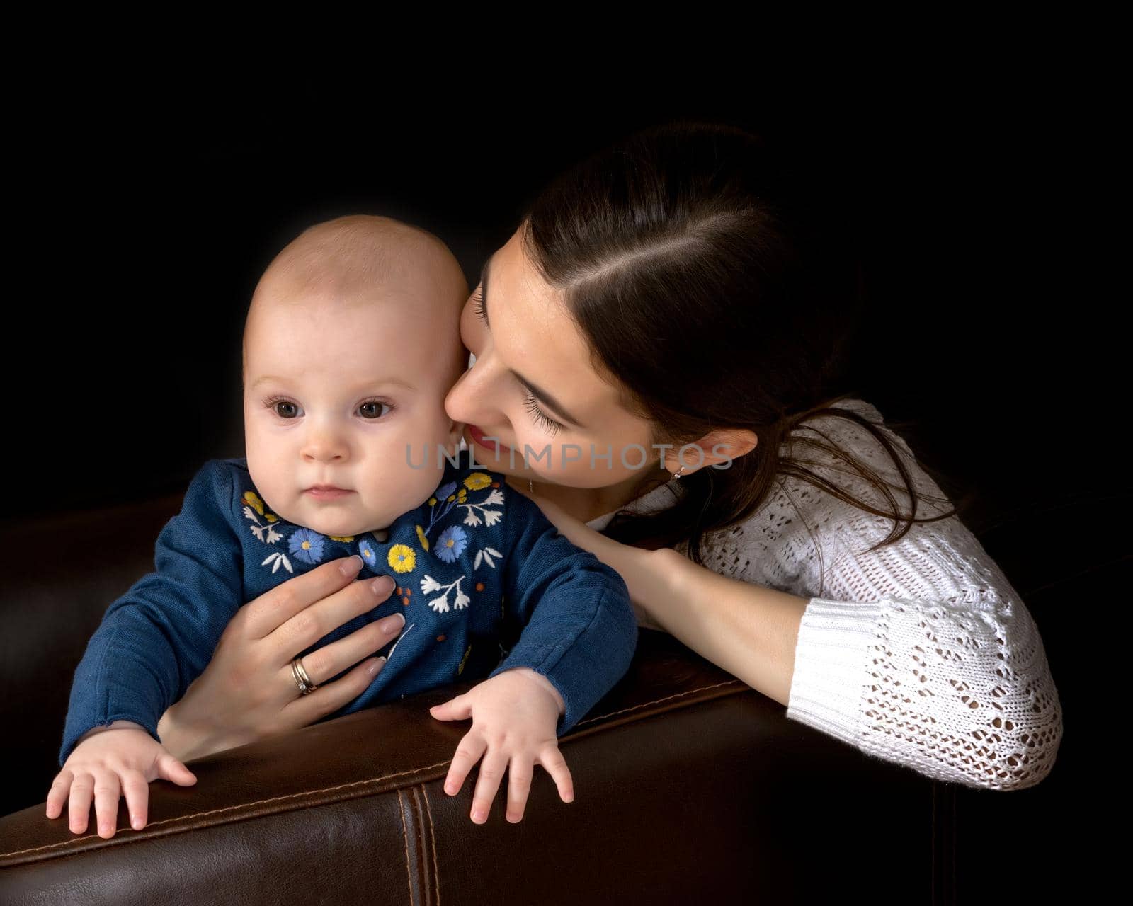 Beautiful young mother with a little daughter in her arms, studio on a black background. The concept of a happy childhood, advertising.