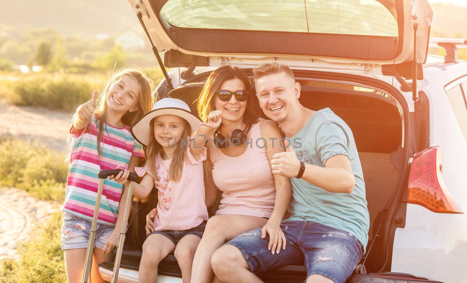 Family are sitting together in the car trunk and smiling and going to travel