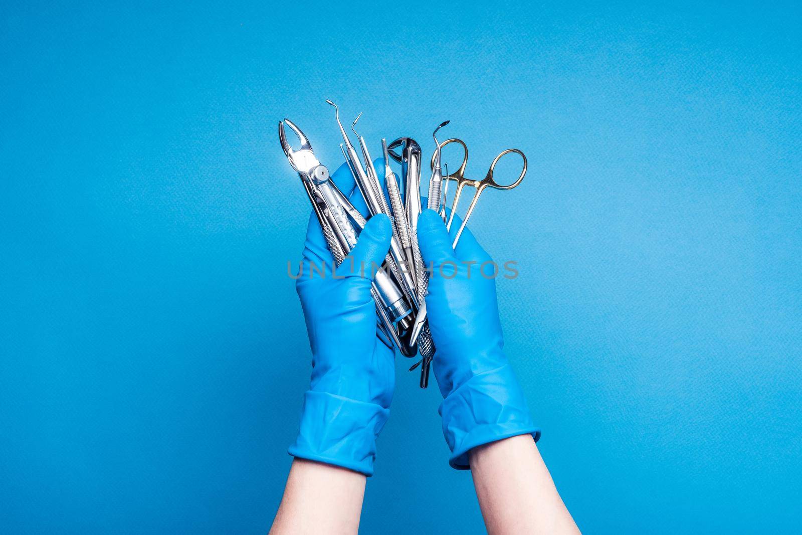 Hands in blue gloves holding dental equipment and metal instruments on blue background