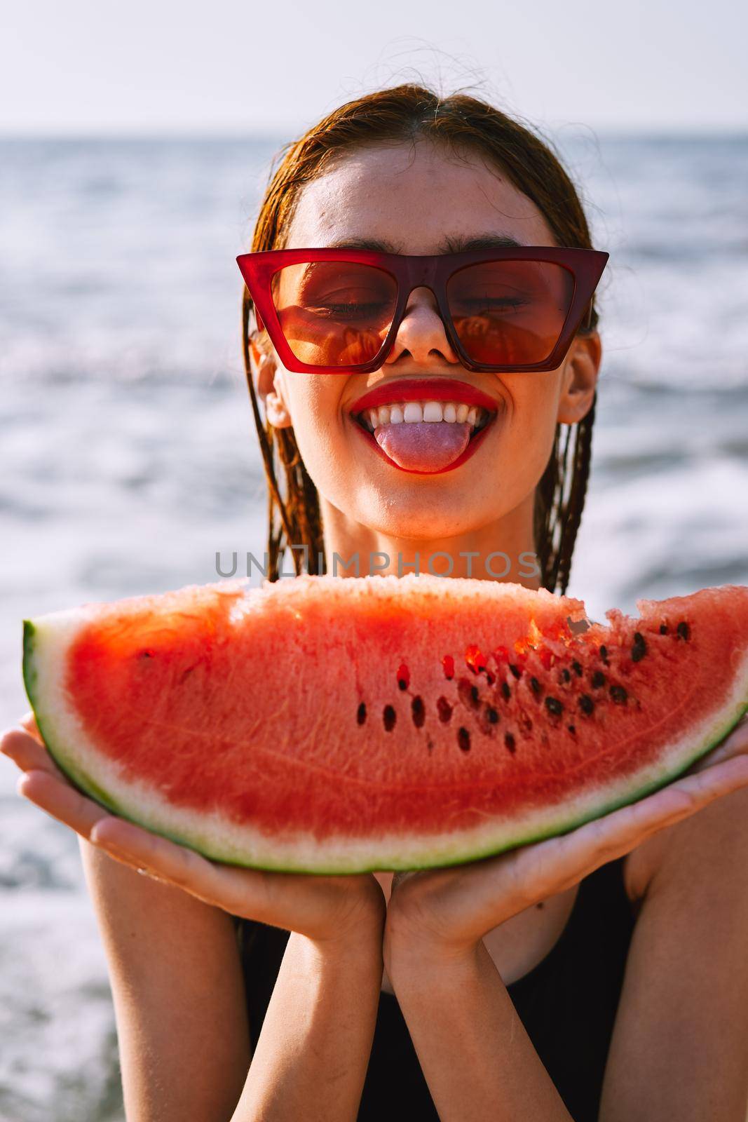 cheerful woman in sunglasses eating watermelon by the ocean. High quality photo