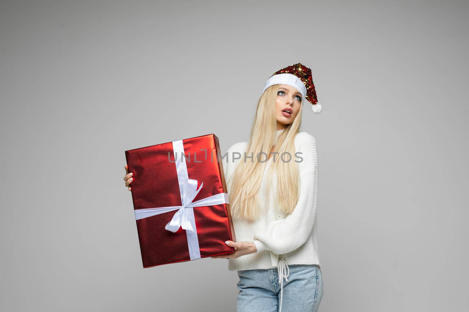 Stock photo of attractive Caucasian woman in white suit with scarf and mittens holding big Christmas gift with white bow.