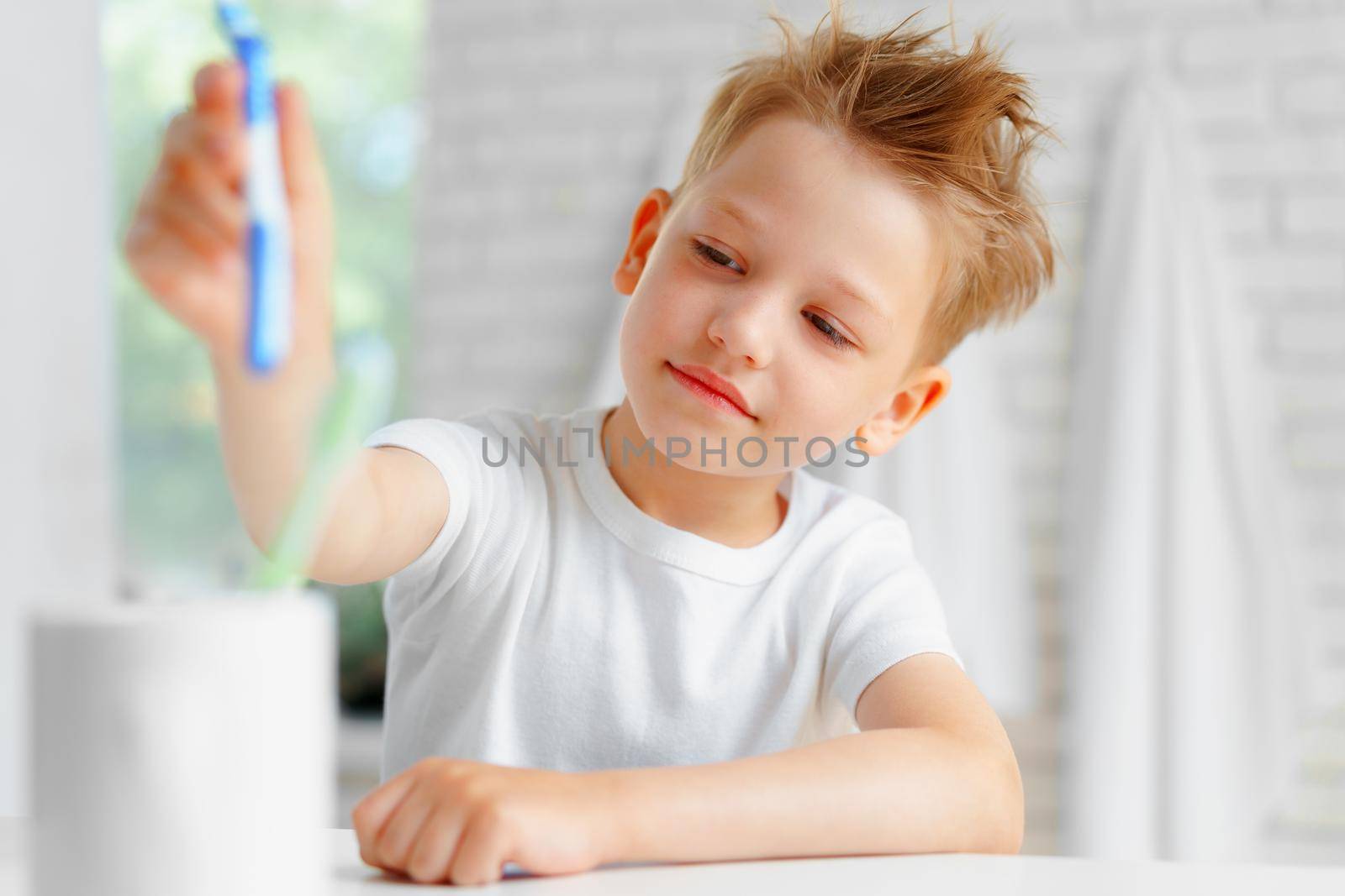 Sleepy boy putting toothbrush in a cup in bathroom