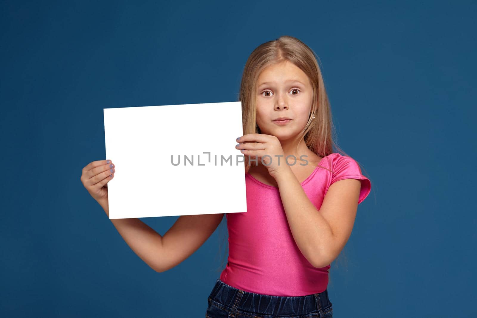 Portrait of adorable blonde little girl on blue background. in pink shirt, holding horizontal white copy space