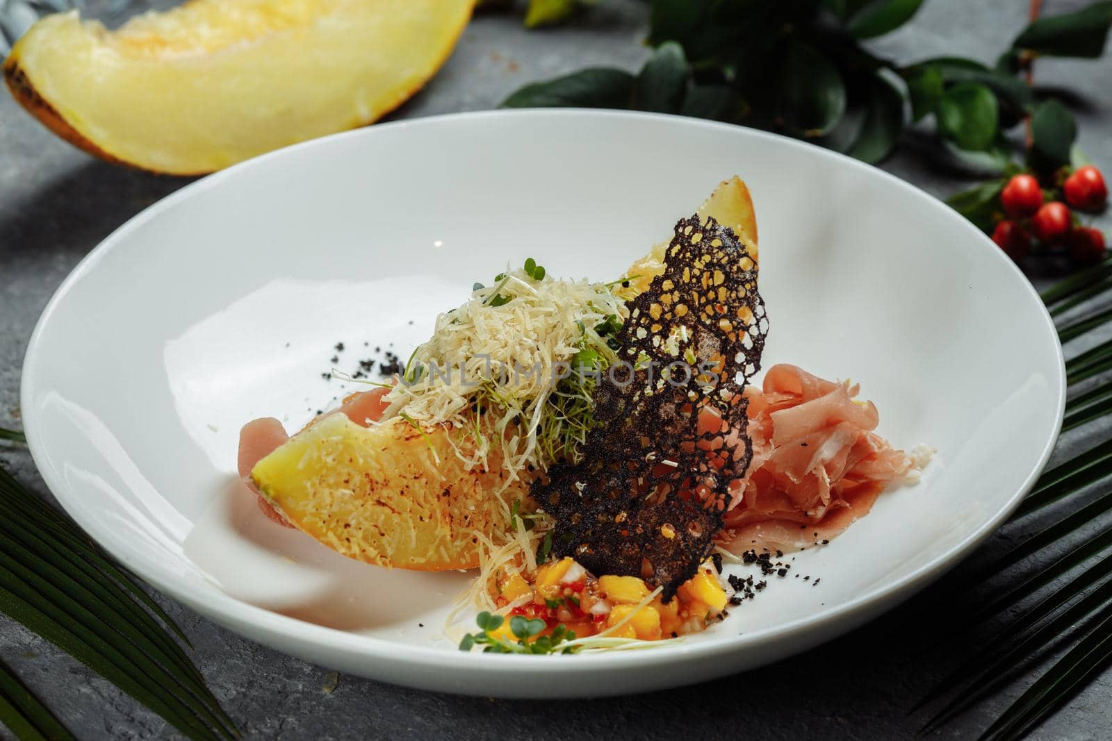 baked melon with parmesan and jamon on a white plate.