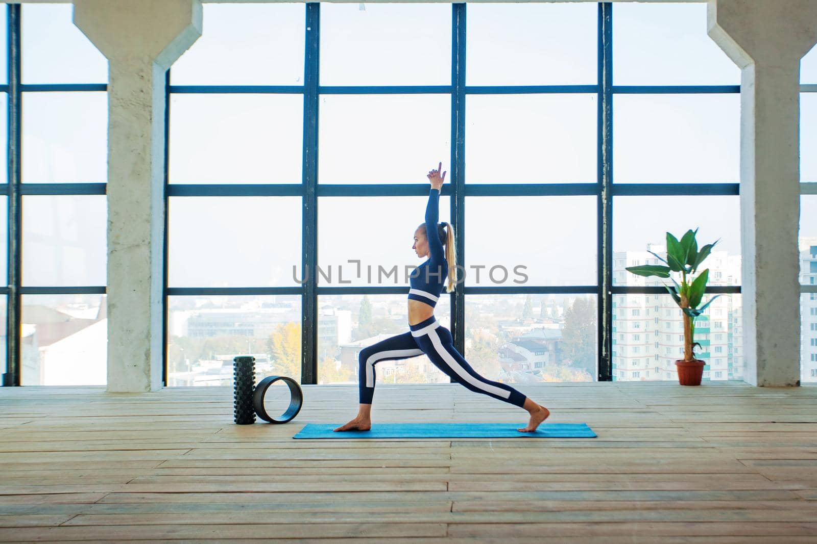 Yoga asana Indoor before a large panoramic window. Sports recreation. Beautiful young woman in yoga pose. Individual sports. by MikeOrlov