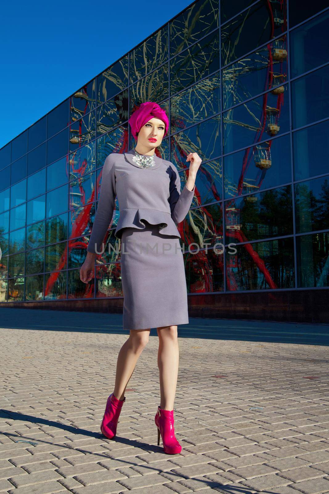 Fashion photo of a beautiful woman in front of a building with reflection of Ferris wheel at summer time