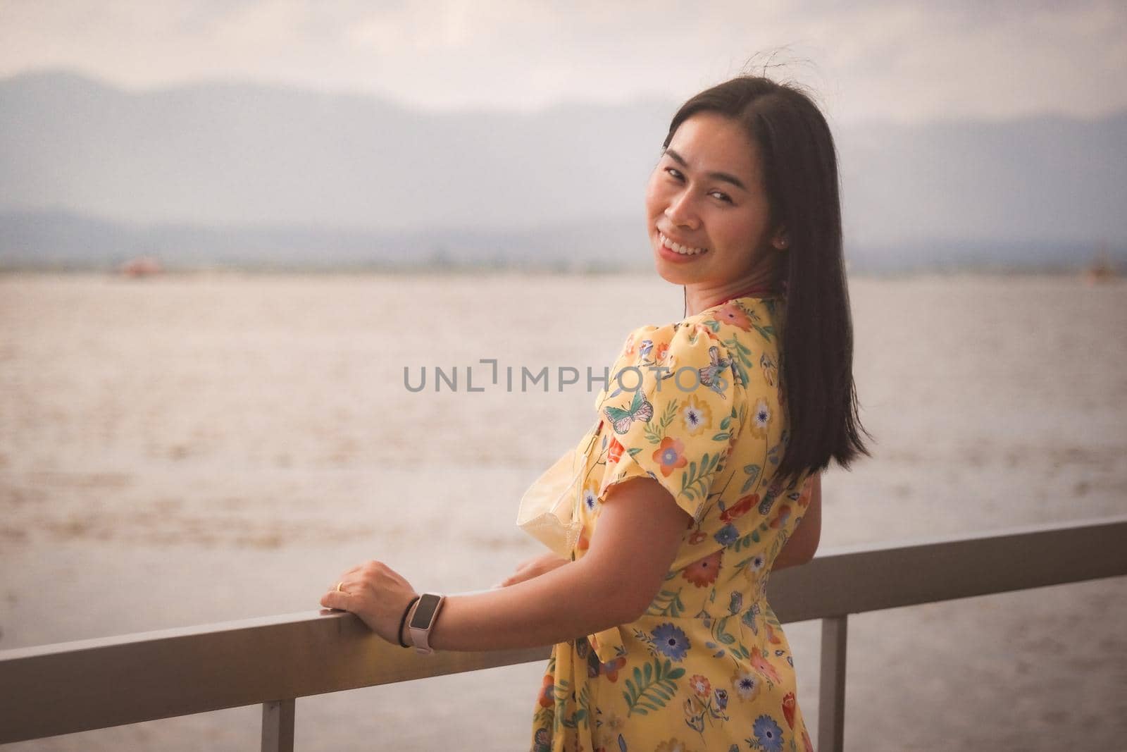 Asian woman tourist enjoying the view and smiling happily to the camera by the lake in vintage tone. Outdoor travel and Nature theme. by TEERASAK